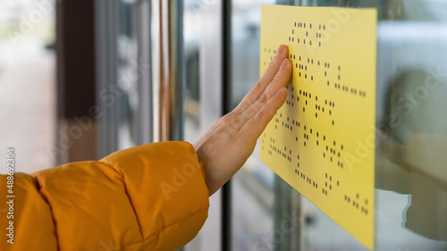 Close-up of a woman reading a braille lettering on a glass door.