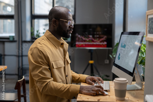 Contemporary young serious economist analyzing finnacial diagrams and graphs on computer screen while sitting by workplace in office