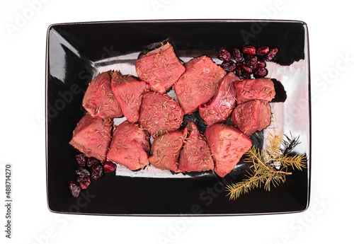 Raw game meat, beef on black plate, isolated. Diced red meat, top view. High quality roe, deer meat.