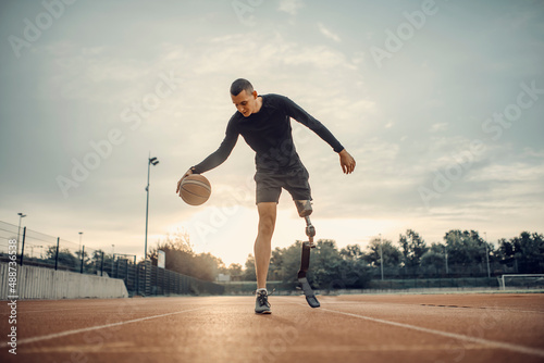 A handicapped sportsman with prosthetic leg dribble the basketball at stadium.