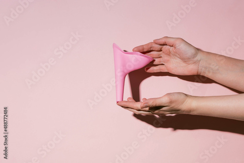 Pink silicone female urinal is a device for urinating in a public toilet. Shadow of a hand on a pink wall.
