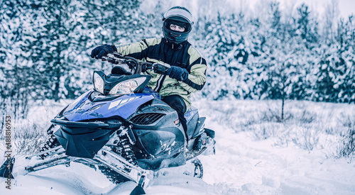 Man driving snowmobile in snowy forest. Man on snowmobile in winter mountain. Snowmobile driving
