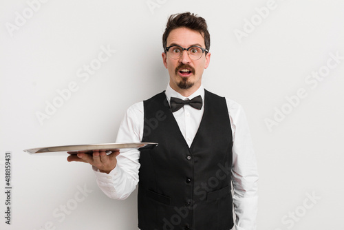 young handsome man looking very shocked or surprised. waiter and tray concept