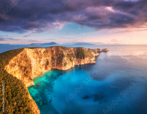 Aerial view of beautiful mountain, blue sea at colorful sunset in summer. Landscape with high rocks, forest, sea bay, beach, azure water, purple sky. Top view of cliffs. Cape Lefkada, Greece. Nature