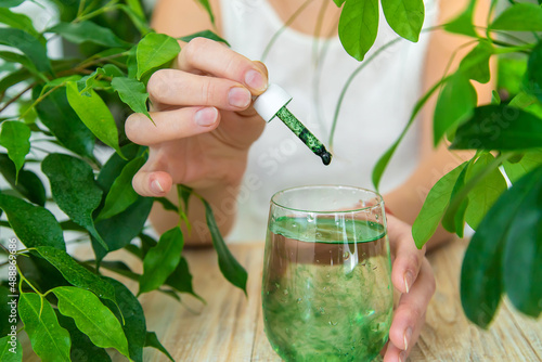 Woman dripping chlorophyll supplement into a glass of water. Selective focus.