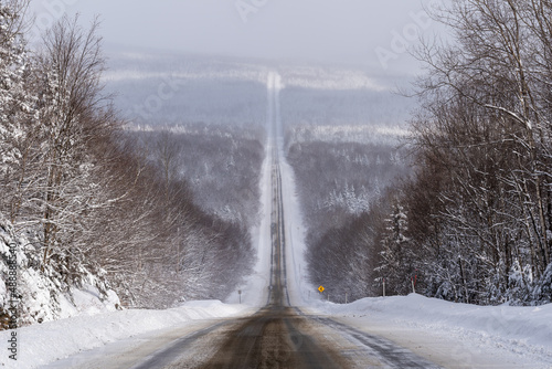 Quebec 216 road, in the region of Chaudière-Appalaches, in winter with a large panoramic view on the snowed forest bordering the partial snowed road.