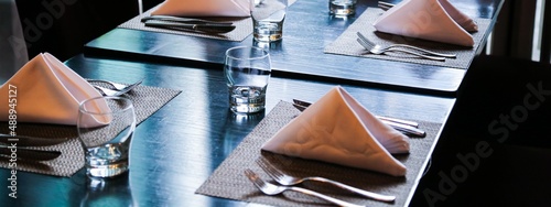 empty drinking glasses and stainless steel knives forks on black wood table with tablemats and folded white napkins