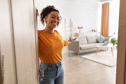 Cheerful African Woman Opening Door Welcoming You Standing At Home