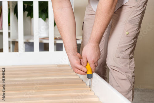 The furniture assembler assembles the bed, twists the screws on the wooden slats, hands with a close-up screwdriver