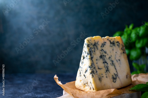 Blue cheese, dor blue or roquefort mold cheese slice on cutting board with basil leaves, lifestyle food.