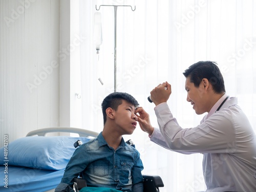 Asian pediatric ophthalmologist who specialize in the diagnosis vision problems. He looking into disabled kid eye before testing eyesight at the hospital