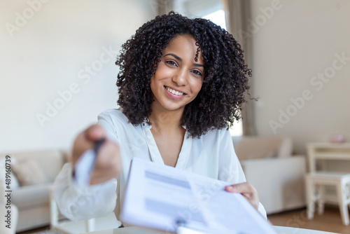 Sign Here. Young smiling confident woman pointing to a contract, sheet of paper, holding a pen, looking and showing it at camera. Presentation, Agreement, Business Concept.