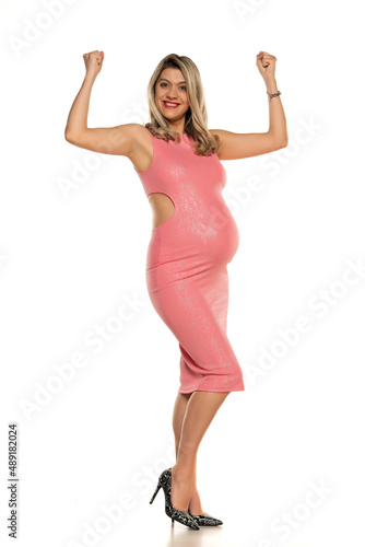 Pregnant woman in tight pink dress showing biceps in studio