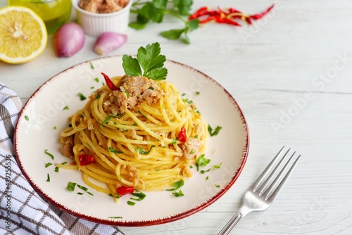 Italian Traditional Dish"Spaghetti al tonno e limone",spaghetti with tuna in olive oil,lemon juice,shallots,olive oil,hot peppers and parleys on plate with white wood background.Copy space