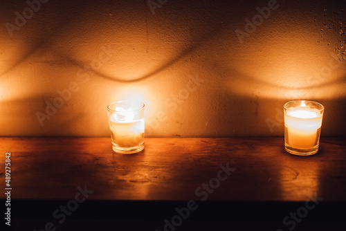 votive candles on wood shelf creating dramatic shadows on white brick wall