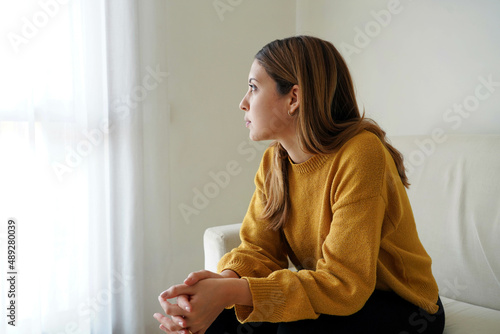 Melancholic sad woman looking through the window at home