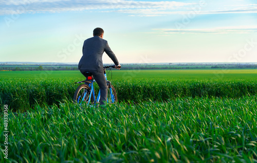one businessman with red folder for reports or documents rides a bicycle through a green grass field, dressed in a business suit, beautiful nature in summer, business concept