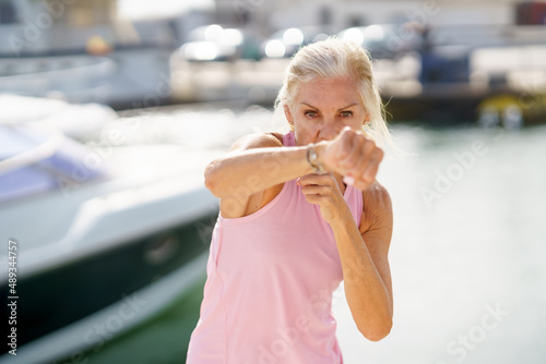 Mature woman doing shadow boxing outdoors. Senior female doing sport in a coastal port