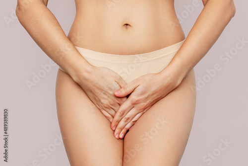 Cropped shot of a young woman in underwear holding her crotch with her hands, suffering from cystitis isolated on beige background. Gynecological problems, genital tract infections. Healthcare concept