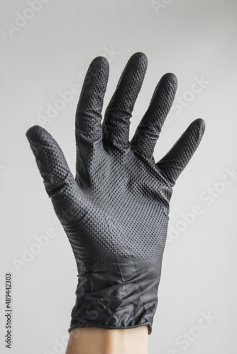 A hand in a black rubber glove on a white background. Personal protective equipment. A man's hand in a black latex glove on a white background close-up. Black gloves isolated on white. 