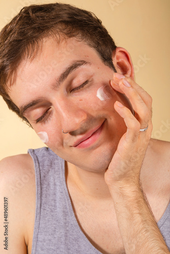 Young and happy man taking care of his skin. Skin care routine. Beautiful model and spa. Isolated beige background.