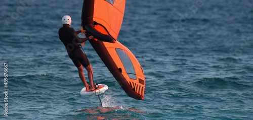 A man is wing foiling using handheld inflatable wings and hydrofoil surfboards in a blue ocean, rider on a wind wing board, surf the waves