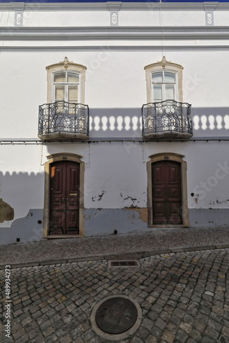Shadow line-whitewashed facade of Neoclassical townhouse-metal railing balconies-wooden doors. Tavira-Portugal-118