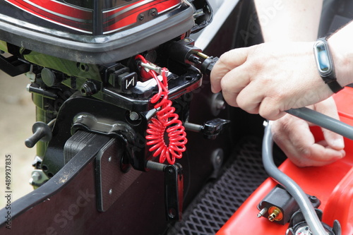 Fuel hose connection to the outboard motor on boat transom closeup with safety rope on plastic fuel tank background.