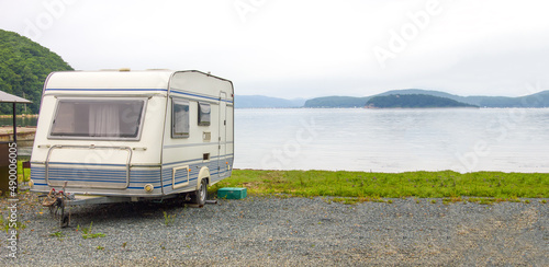 Russia, Vladivostok, August 18, 2020: Trailer motor home on beach at sunset. Leisure mobile camping home for tourists overlooking the blue lake and cape. Adventure relaxing travel on caravan van