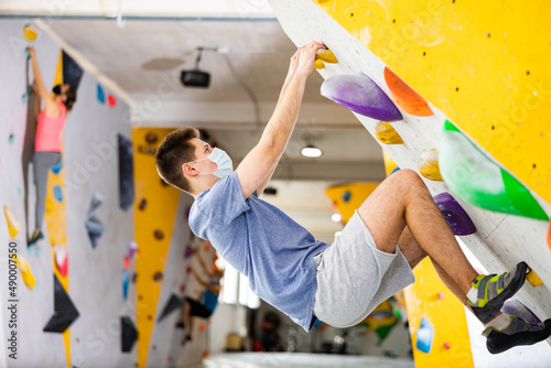 Male mountaineer in protective mask climbing artificial rock wall without his belay indoors