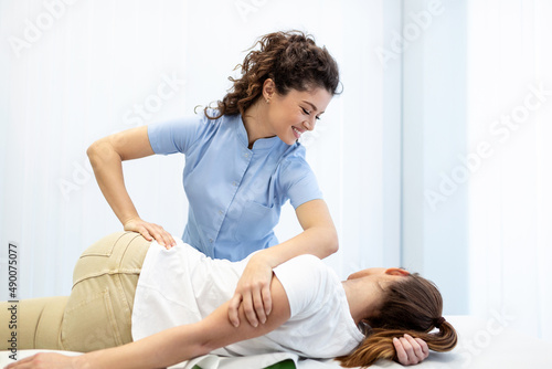 Young doctor chiropractor or osteopath fixing lying womans back with hands movements during visit in manual therapy clinic. Professional chiropractor during work