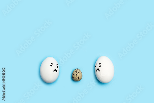 Un huevo de codorniz y huevos de gallina blancos alrededor sobre un fondo celeste liso y aislado. Vista superior. Copy space, Concepto: Discriminación, Acoso