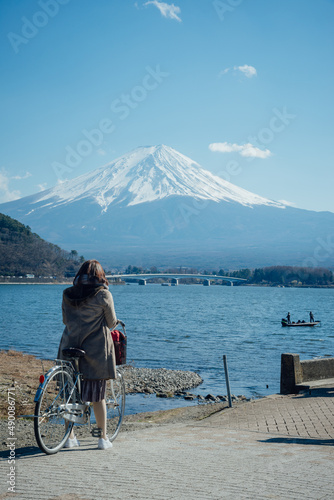 A woman was parking a bicycle and taking a photo at Lake Kawaguchi with Mount Fuji behind, Yamanashi, Japan.