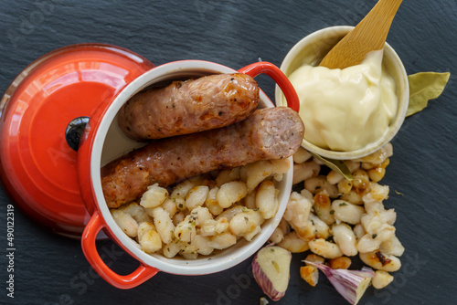 Sausages with white beans, in catalan butifarra with mongetes with allioli sauce, typical dish from catalonia, spain. slate plate and wooden spoon.