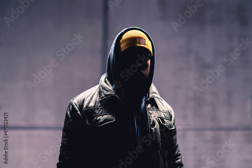 Hooded criminal in dark. Mystery man with hood. Gangster in urban street. Hooligan in hoodie. Stalker with hidden face. Unknown suspicious thief, burglar, hacker or terrorist with grunge background.