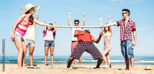 Multicultural friends group having fun together with limbo game at beach vacation - Summer joy life style concept with young multi ethnic people playing on spring break vacation - Bright filter