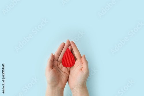 Concept of give blood donation, blood transfusion. Hands woman hold drop of blood on blue background. World hemophilia day.