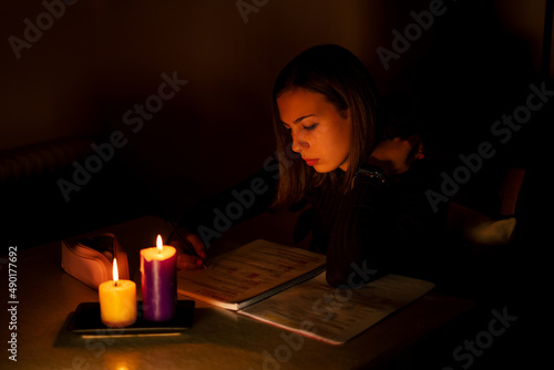 Young Caucasian woman studying by candlelight - blackout concept