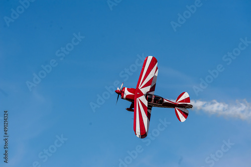 Red and white biplane flying against a blue sky
