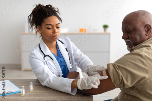 Black Mature Man Getting Vaccinated, Doctor Applying Adhesive Bandage