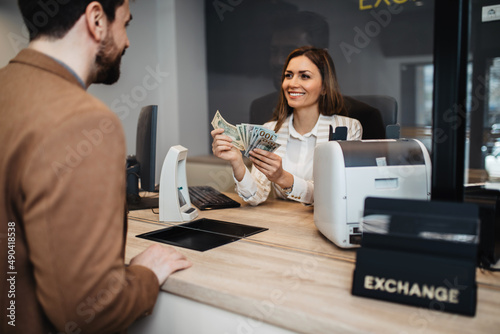 Attractive European businesswoman working in exchange office. She is giving cash money to male customer.