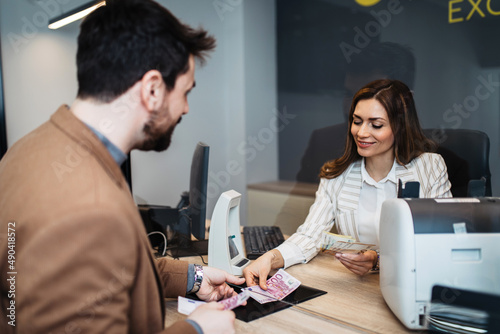 Attractive European businesswoman working in exchange office. She is giving cash money to male customer.