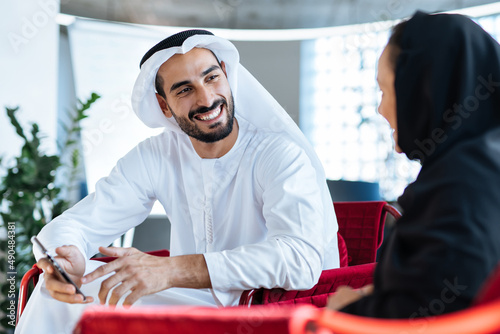 Man and woman with traditional clothes working in a business office of Dubai. Portraits of successful entrepreneurs businessman and businesswoman in formal emirates outfits. 