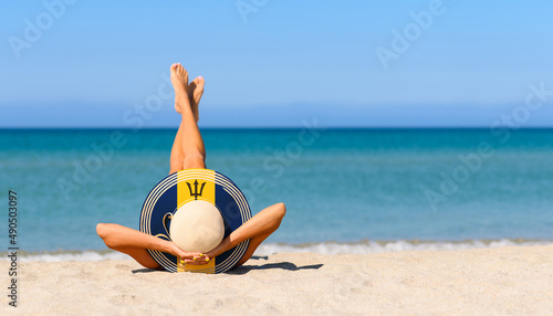 A slender girl on the beach in a straw hat in the colors of the Barbados flag. The concept of a perfect vacation in a resort in the Barbados. Focus on the hat.