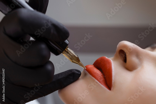 Cosmetologist makes permanent makeup on a woman's face. Specialist applies a tattoo on the patient's lips close-up