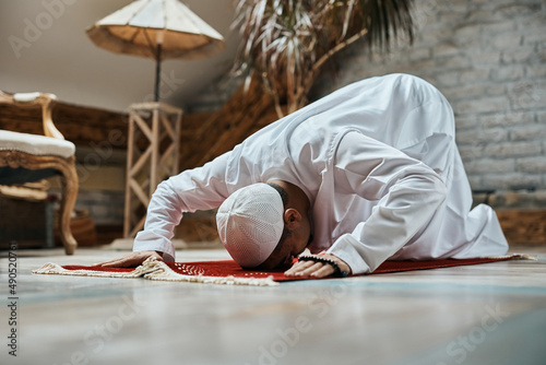 Religious Muslim man prostrating to God while praying at home.