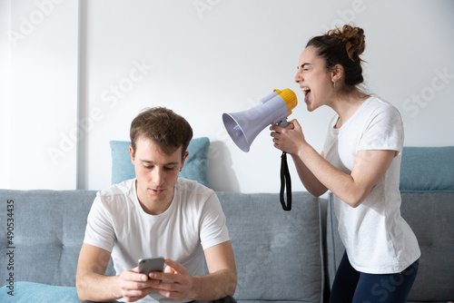 Cohabitation problems concept. Woman shouting on megaphone and boyfriend ignoring her.