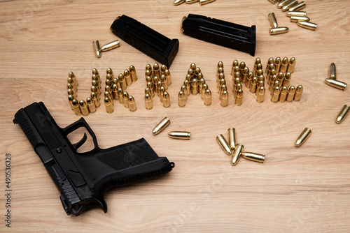 Napis ukraine ułożony z naboi na stole, wokół rozrzucone naboje, broń krótka oraz dwa załadowane magazynki obok