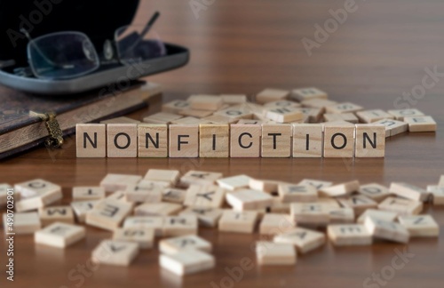 nonfiction word or concept represented by wooden letter tiles on a wooden table with glasses and a book