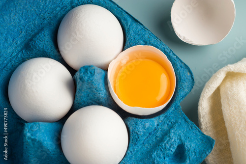 Close-up of chicken fresh eggs in eco-packaging on a blue background. Broken egg with yolk in the shell. Farm natural products. Top view.